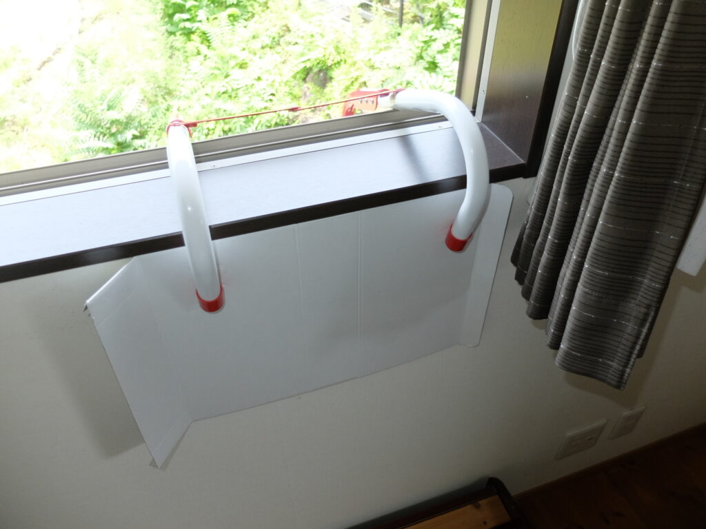 窓枠にこのように引っ掛けて使います。
壁厚さは15~26cmの範囲であれば使用可能です。
訓練では、壁に傷がつかないように段ボールを挟んでいます。