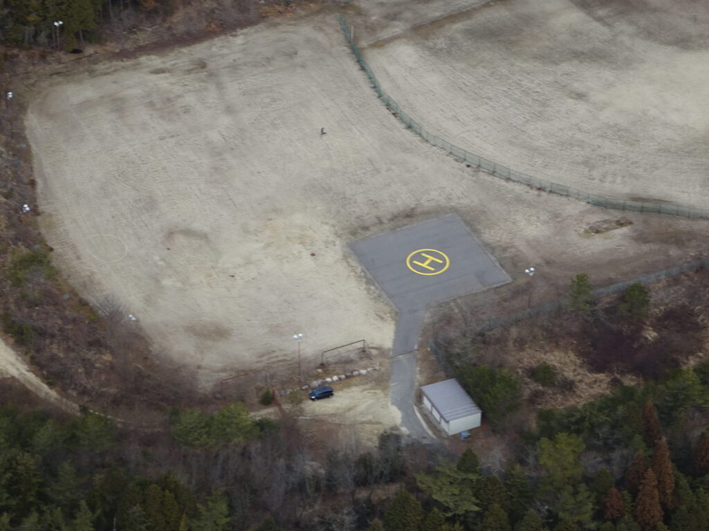 某所の場外離着陸場はグラウンドの敷地を利用して整備されているが、乾燥時は散水が必要。